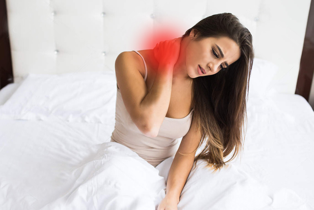 Young woman sitting on the bed with pain on neck